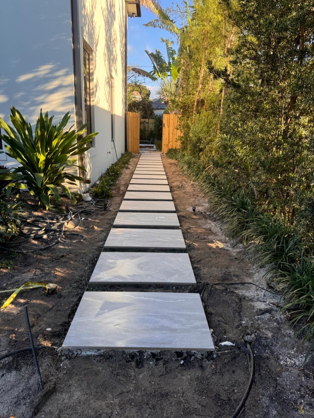 Large-format paver walkway installation beside a modern white house at golden hour
